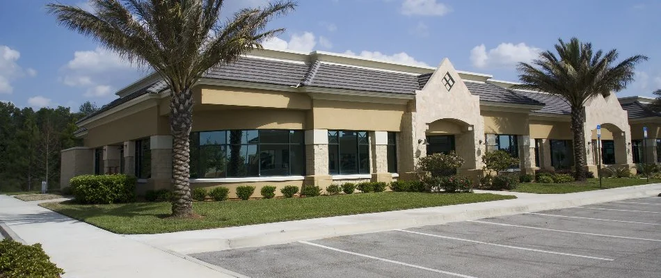 Commercial building in West Palm Beach, FL, with a parking lot, grass, and plants.